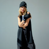 Person wearing black gloves and a beanie with a logo on a gray background