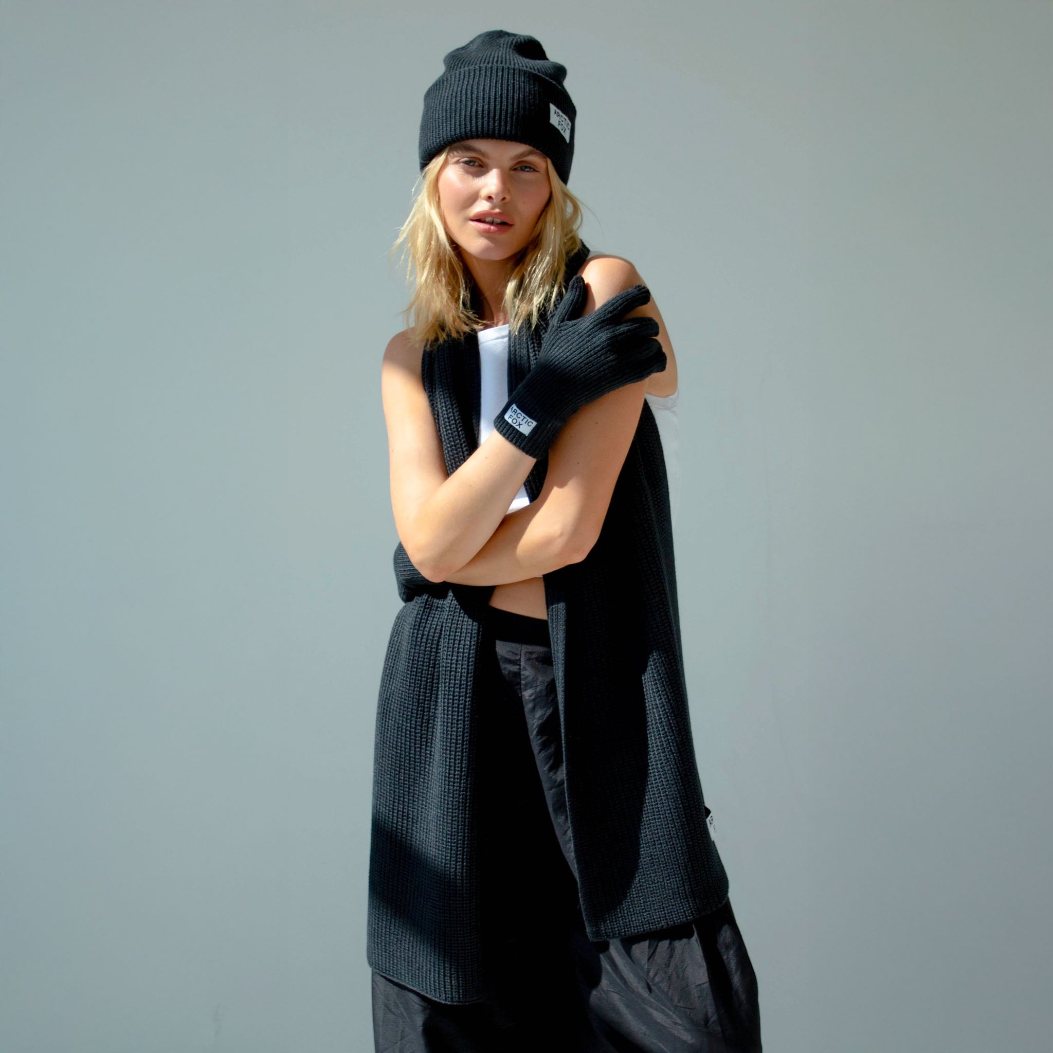 Person wearing black gloves and a beanie with a logo on a gray background