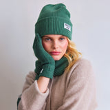 Person wearing a green knit hat and scarf with 'Arctic Fox' branding on a light gray background