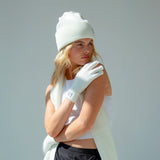 Woman wearing a white beanie, gloves, and scarf against a light gray background