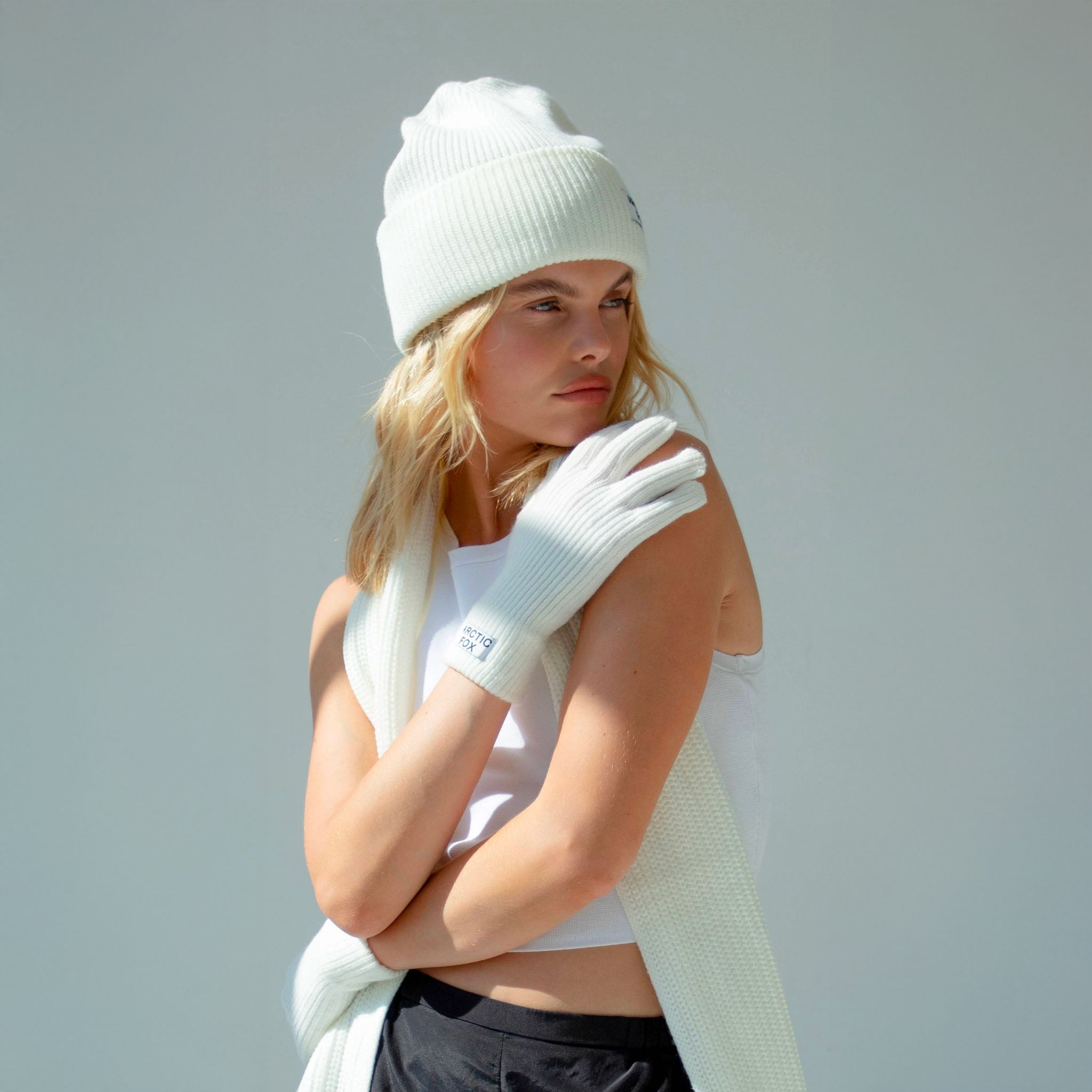 Woman wearing a white beanie, gloves, and scarf against a light gray background