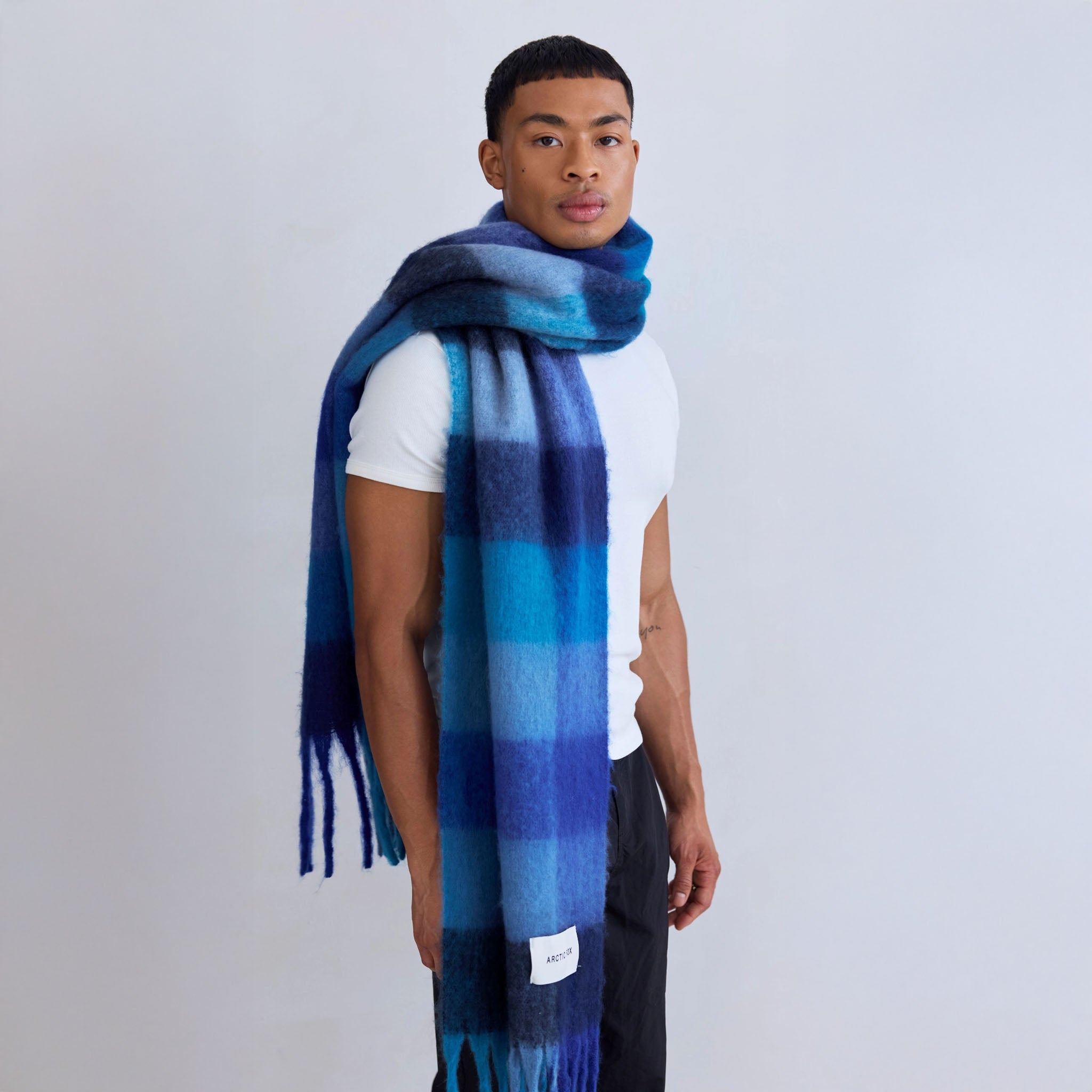 Man wearing a blue plaid scarf on a plain background