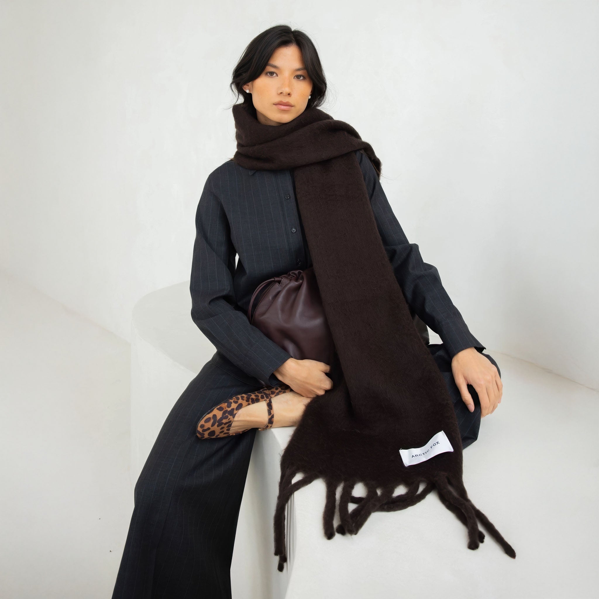 Model wearing a dark brown scarf with a brand label Arctic Fox, sitting on a white surface.
