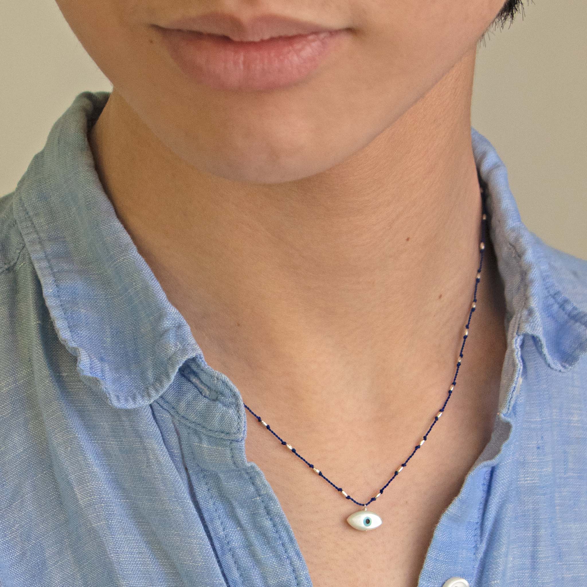 Person wearing a blue shirt with See Real Flowers Evil Eye Necklace in blue.