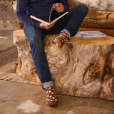 Person sitting on a wooden log bench reading a book, wearing polka dot socks.