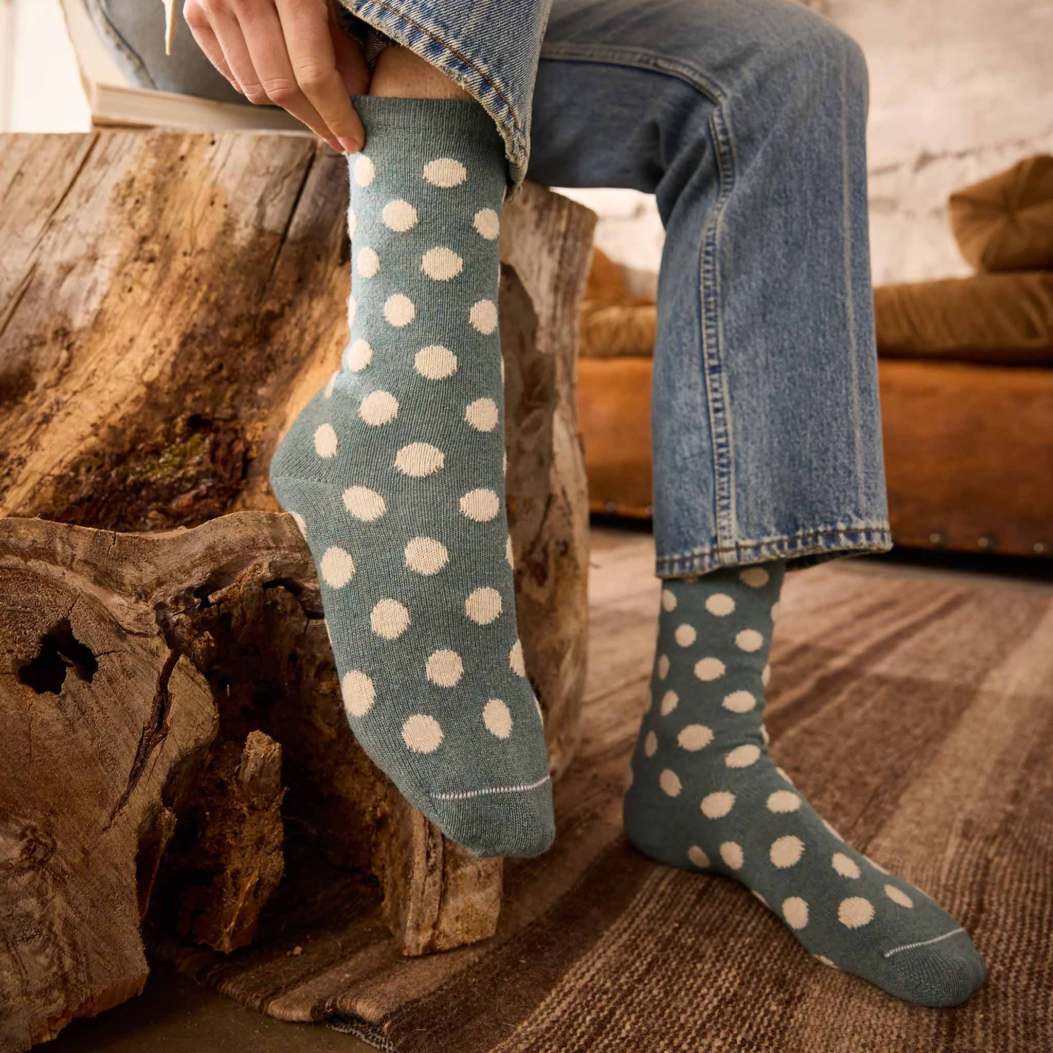 Person wearing blue socks with white polka dots sitting on a wooden log.