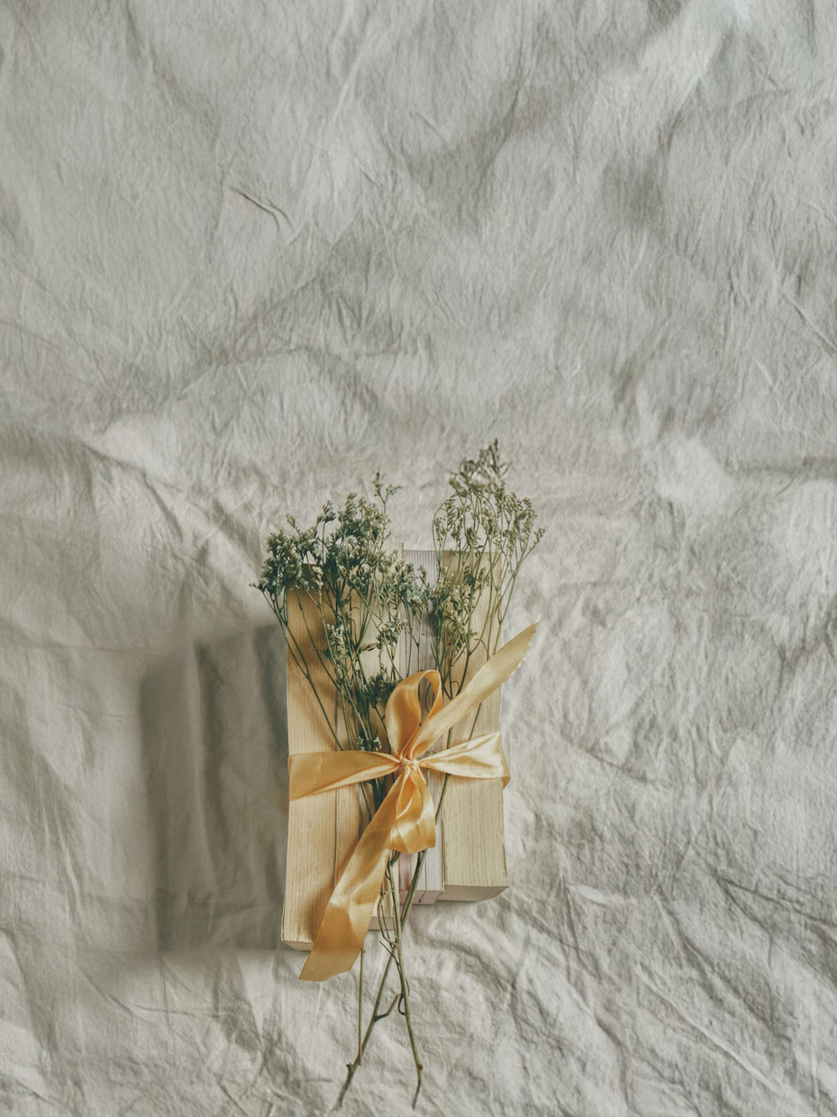Books wrapped with a yellow ribbon and small bouquet on a textured light gray surface
