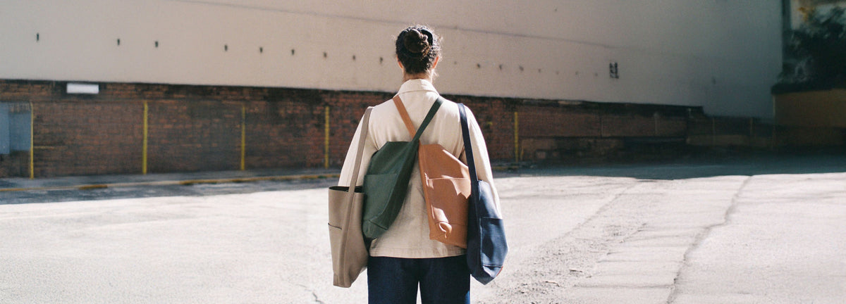Person holding 4 Bonarda shoulder bags in various colors in an urban setting
