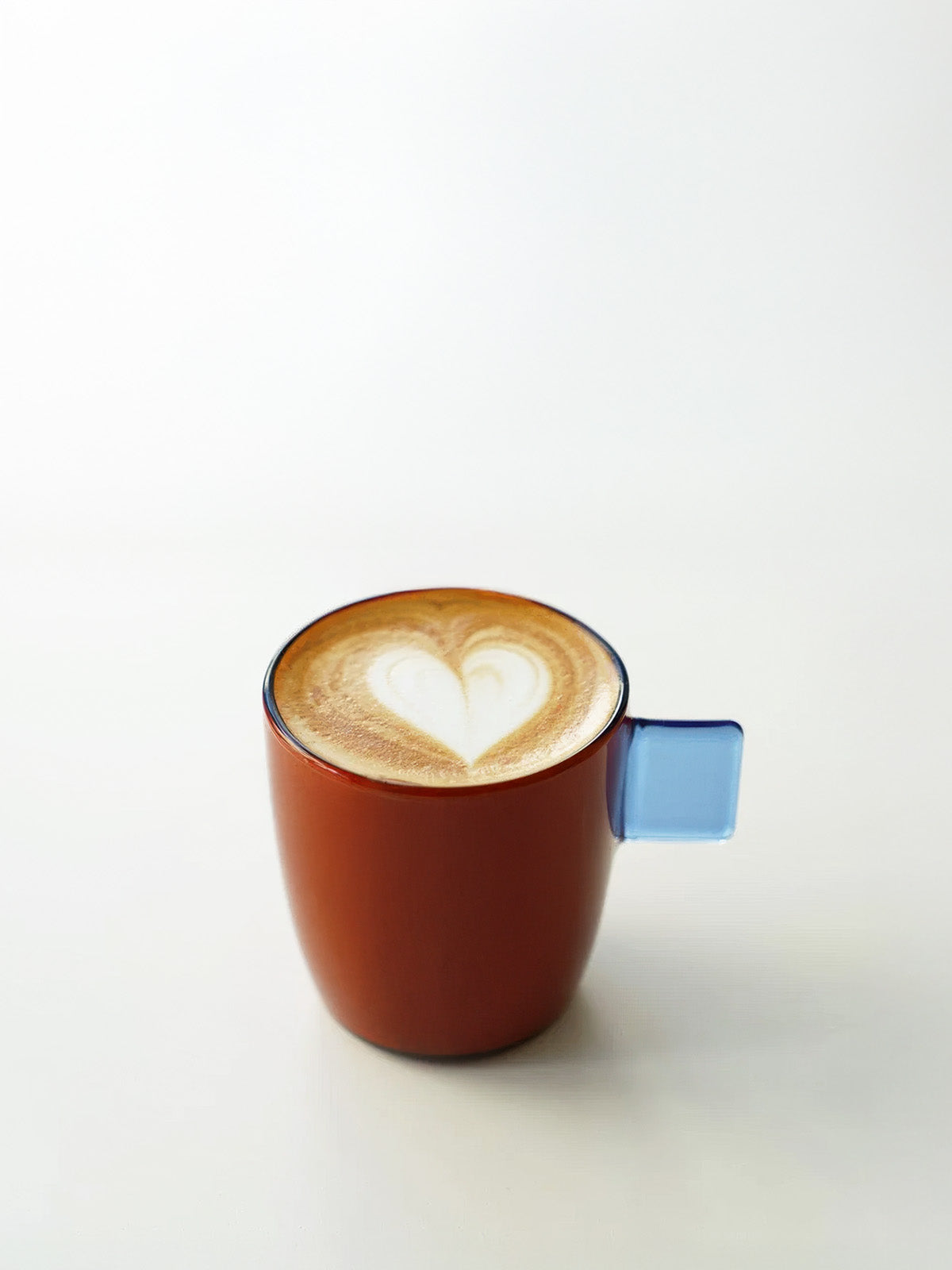 Cappuccino with a heart-shaped foam design in a glass amber cup on a white background