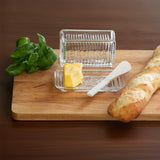 Butter dish with a stick of butter, a baguette, and basil leaves on a wooden board.