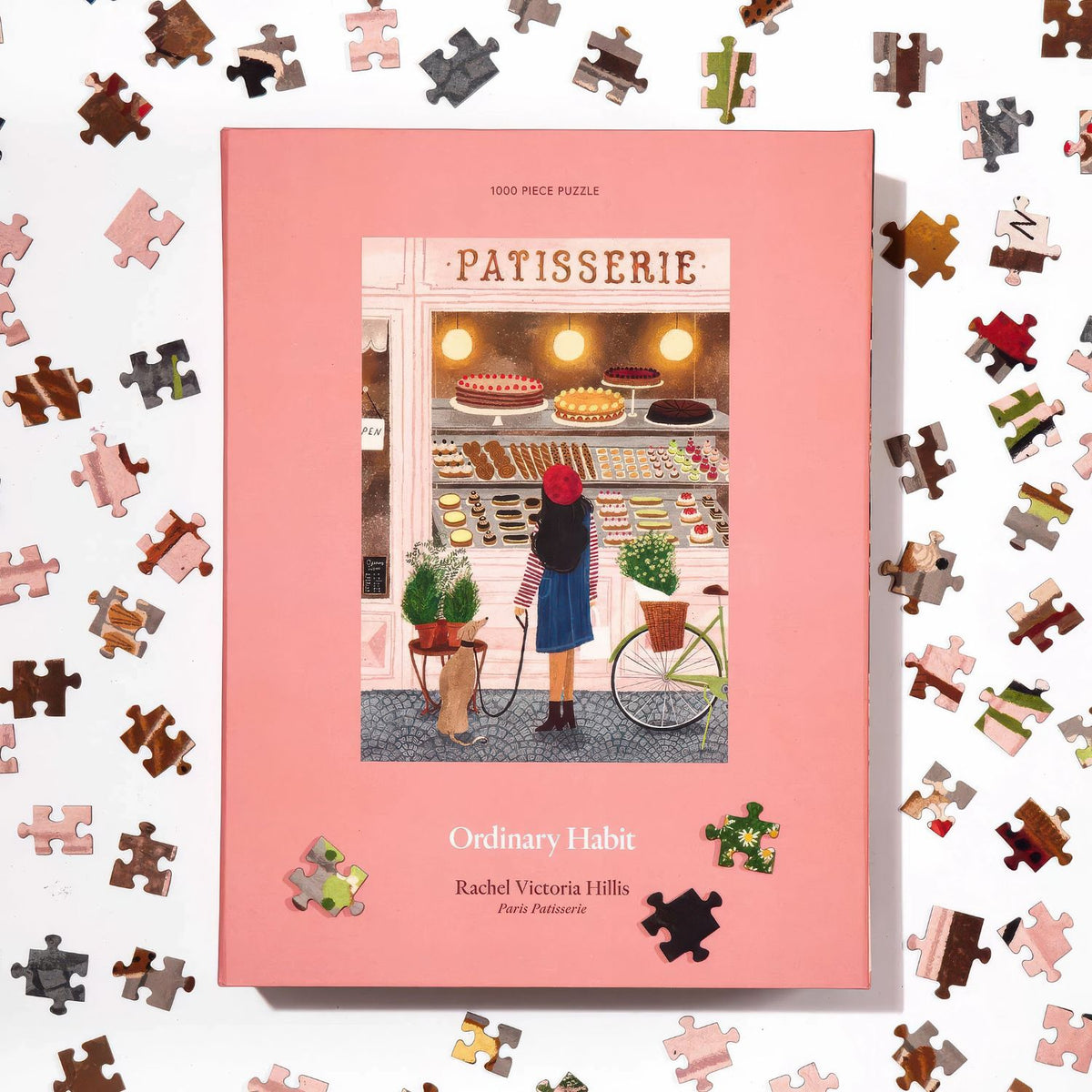 Top view of Ordinary Habit's 1000pc Paris Patisserie puzzle box with puzzle pieces on a white background
