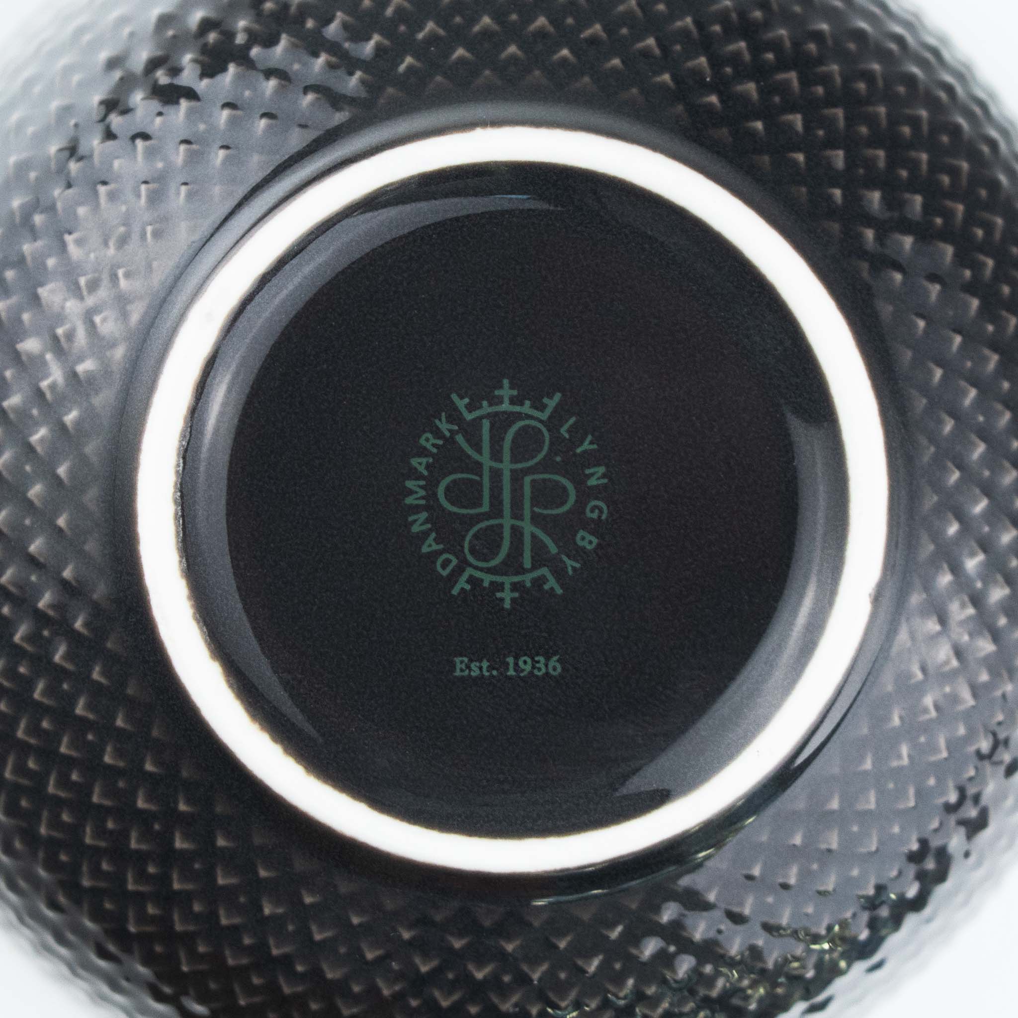 Close-up of a black ceramic product with a brand logo and text on a textured surface.