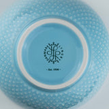 Close-up of a turquoise ceramic bowl with a brand logo and text on a white background