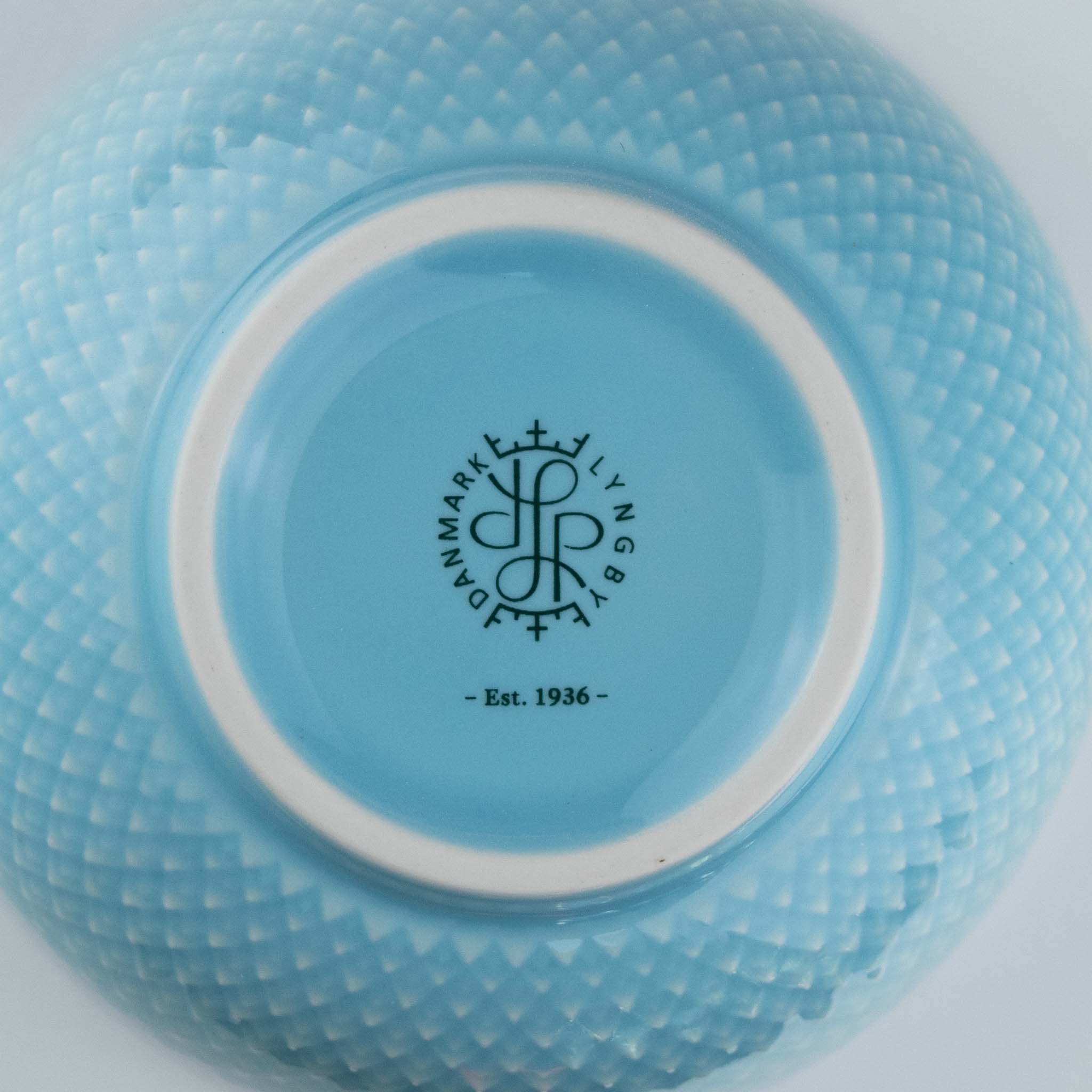 Close-up of a turquoise ceramic bowl with a brand logo and text on a white background