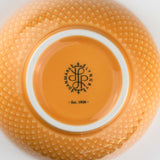 Close-up of an orange-yellow ceramic bowl with a brand logo and text on a white background