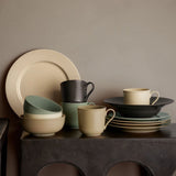Set of ceramic porcelain dinnerware including plates, bowls, and mugs on a dark surface with a neutral background.
