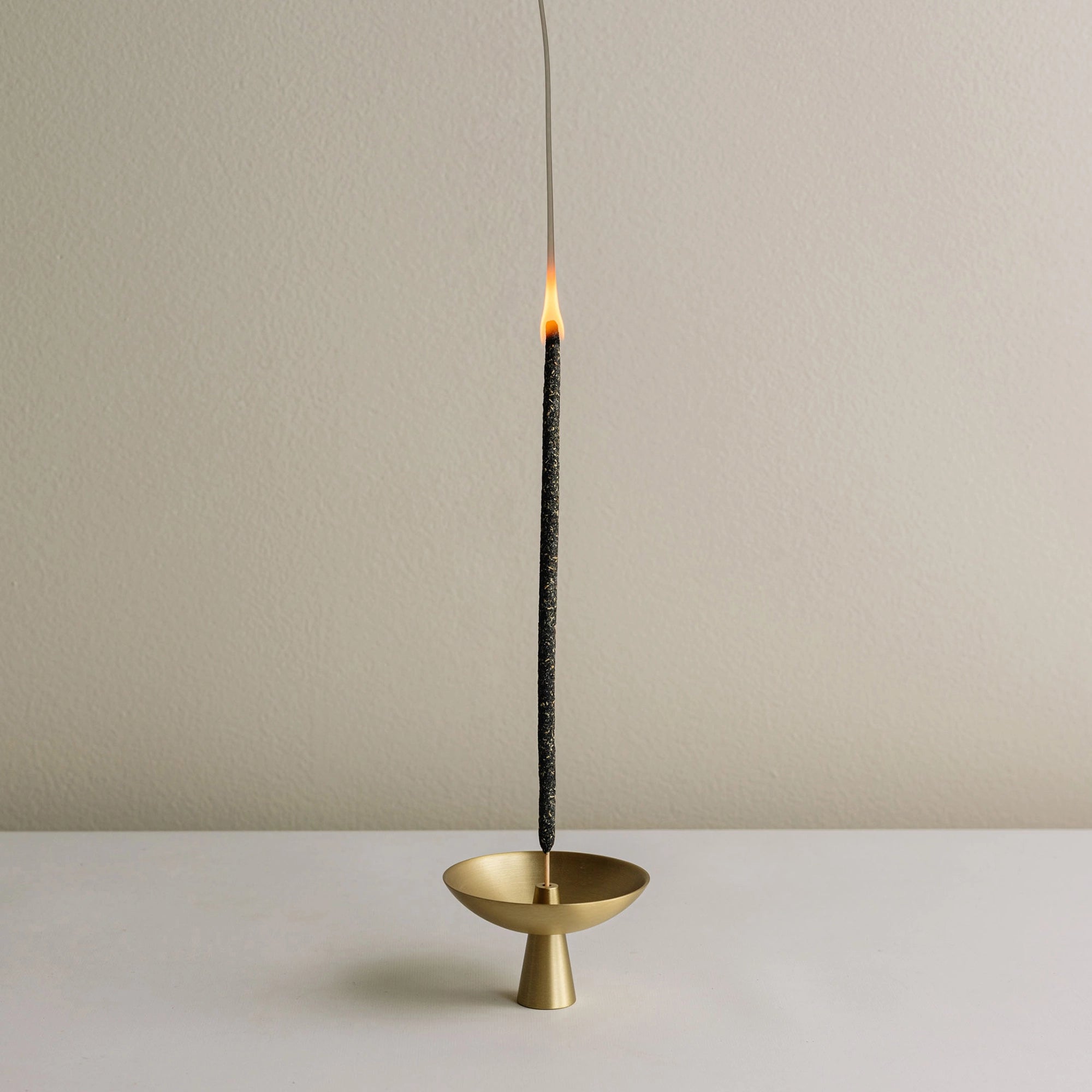 Incense stick burning in a gold holder on a neutral background