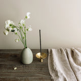 Vase with white flowers, incense stick holder, and beige towel on a wooden surface.