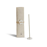 Incense stick holder with a cylindrical beige container and a white flower-shaped weight on a white background
