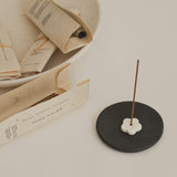 Incense stick on a black ceramic holder with books in the background