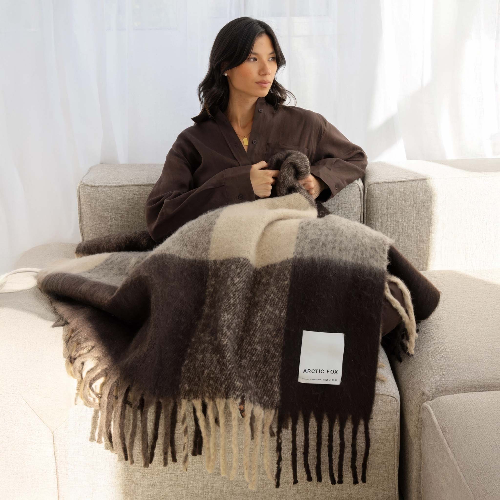 Woman sitting on a couch with a Plaid throw with brown, beige, and white pattern with label Arctic Fox