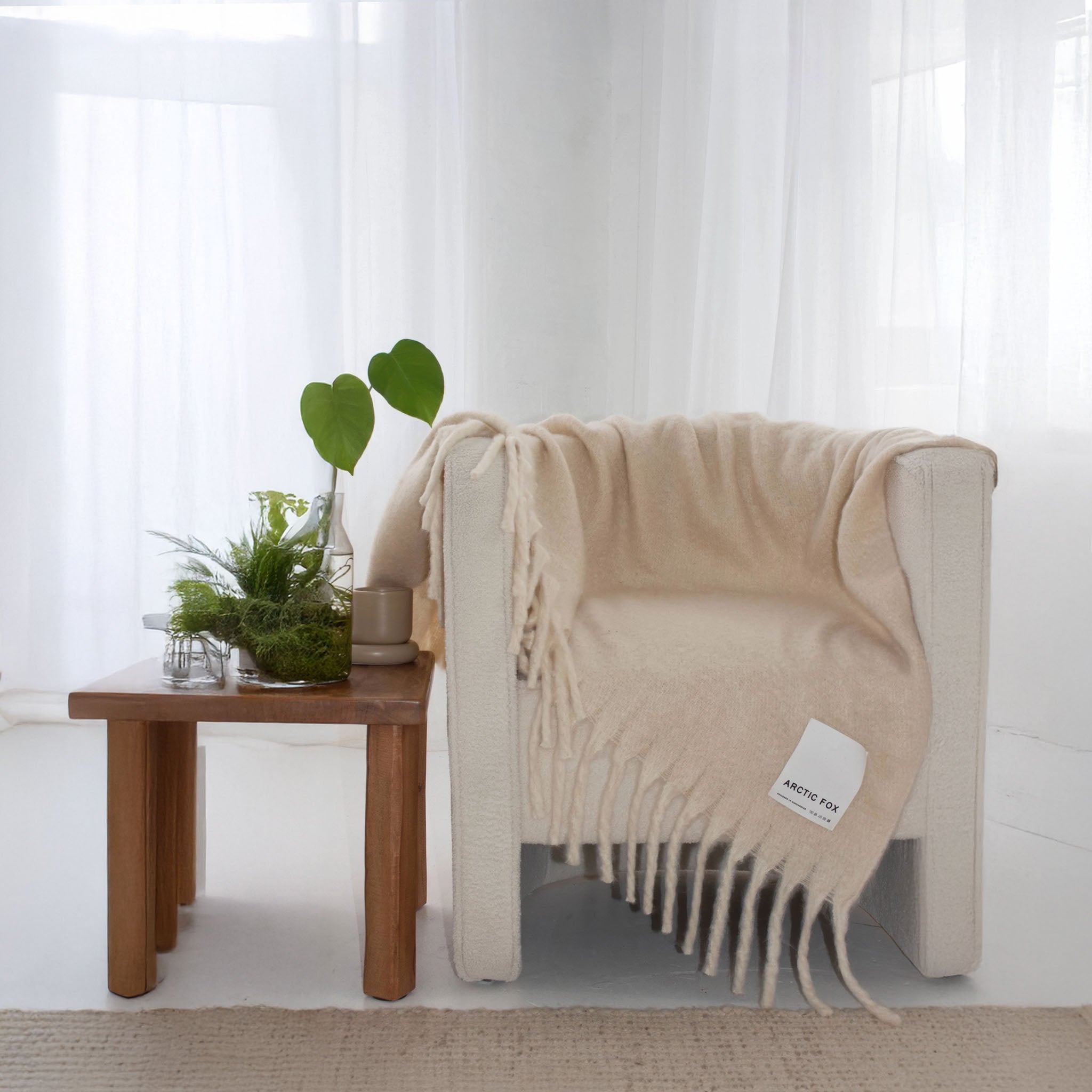 Beige throw with brand label Arctic Fox draped over a chair next to a wooden table with plants, in a bright room.