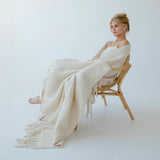 Model sitting on a chair with a beige throw draped over her, against a plain background
