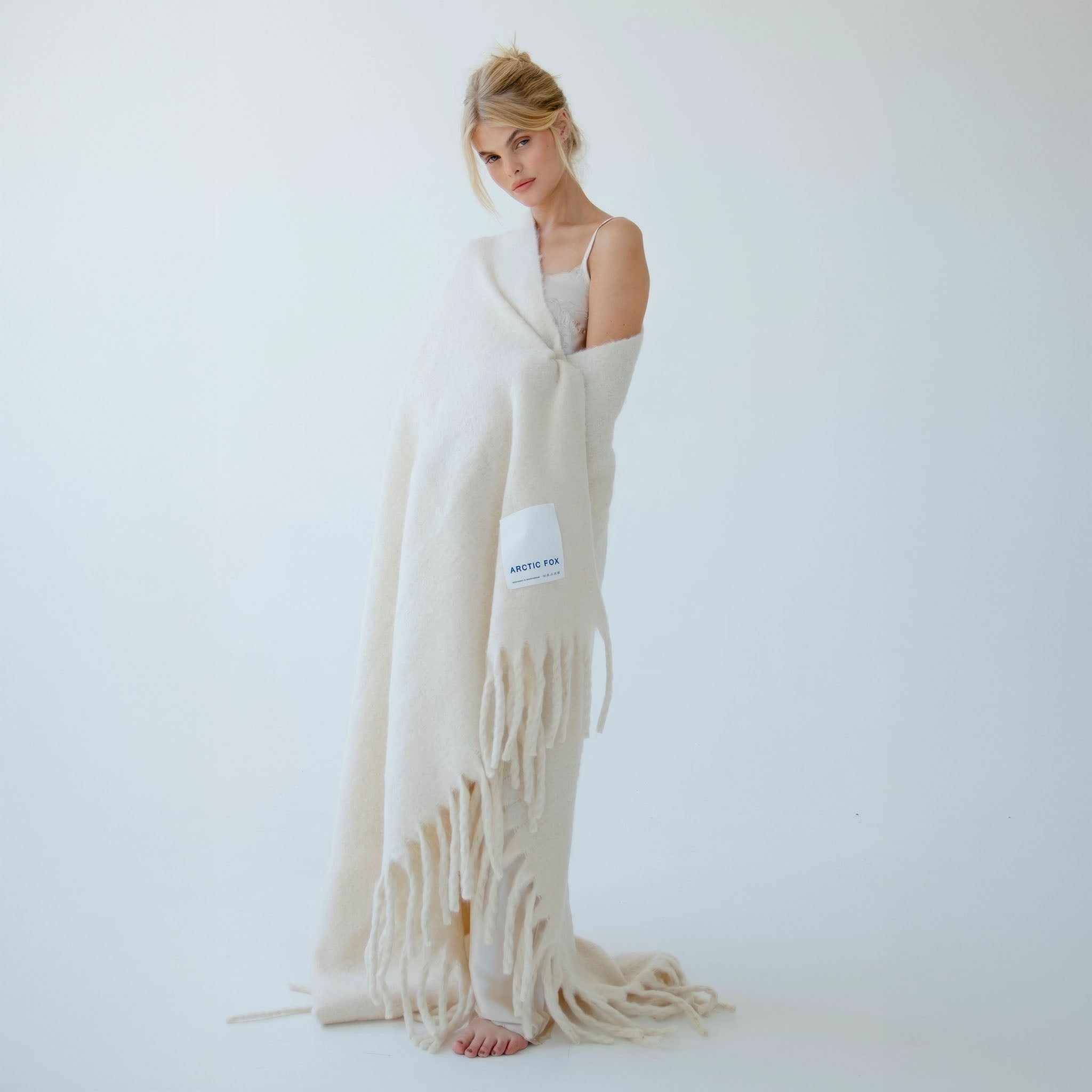 Model wrapped in a long, beige blanket with a visible brand logo Arctic Fox on a light background