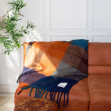 Colorful plaid blanket draped over a brown leather sofa with a white wall and plant in the background