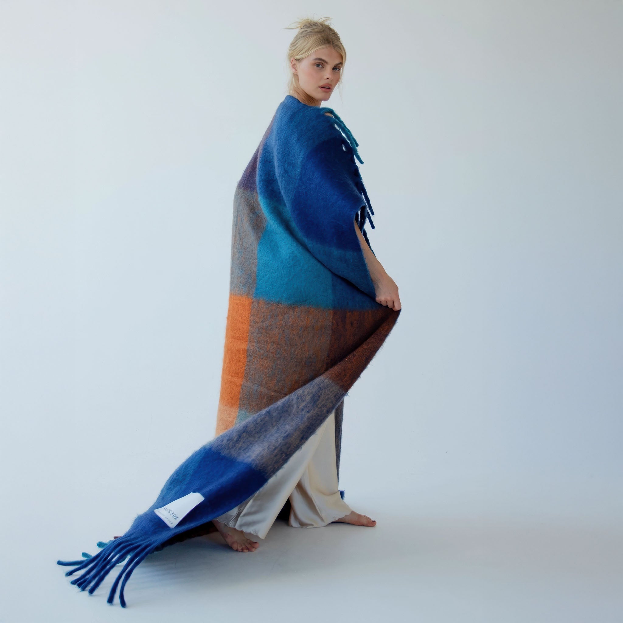 Model wrapped up in a colorful woven blanket against a white background