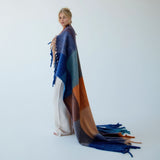 Model wrapped up in a colorful woven blanket against a white background