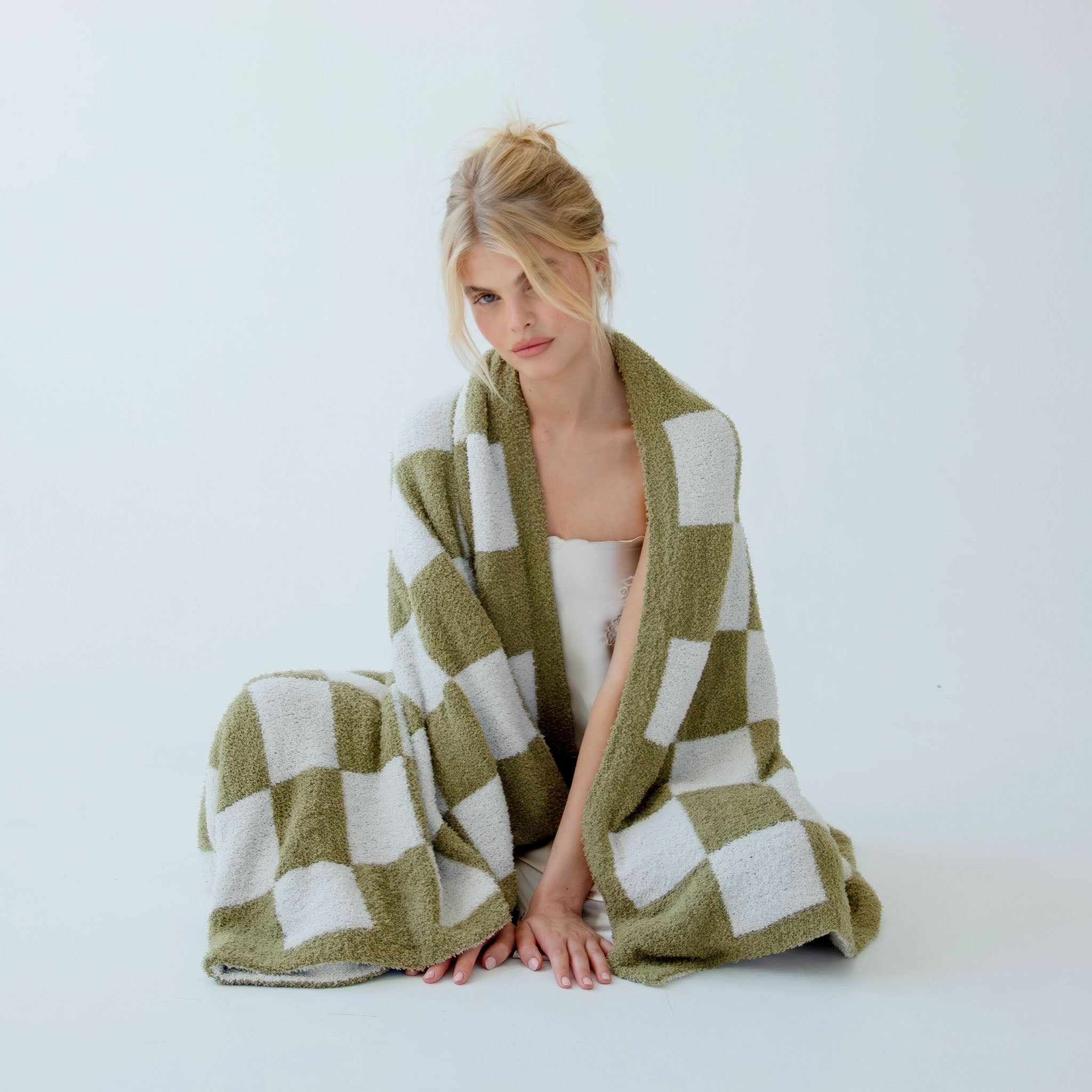 Model wrapped in a moss green and white checkered blanket on a light background
