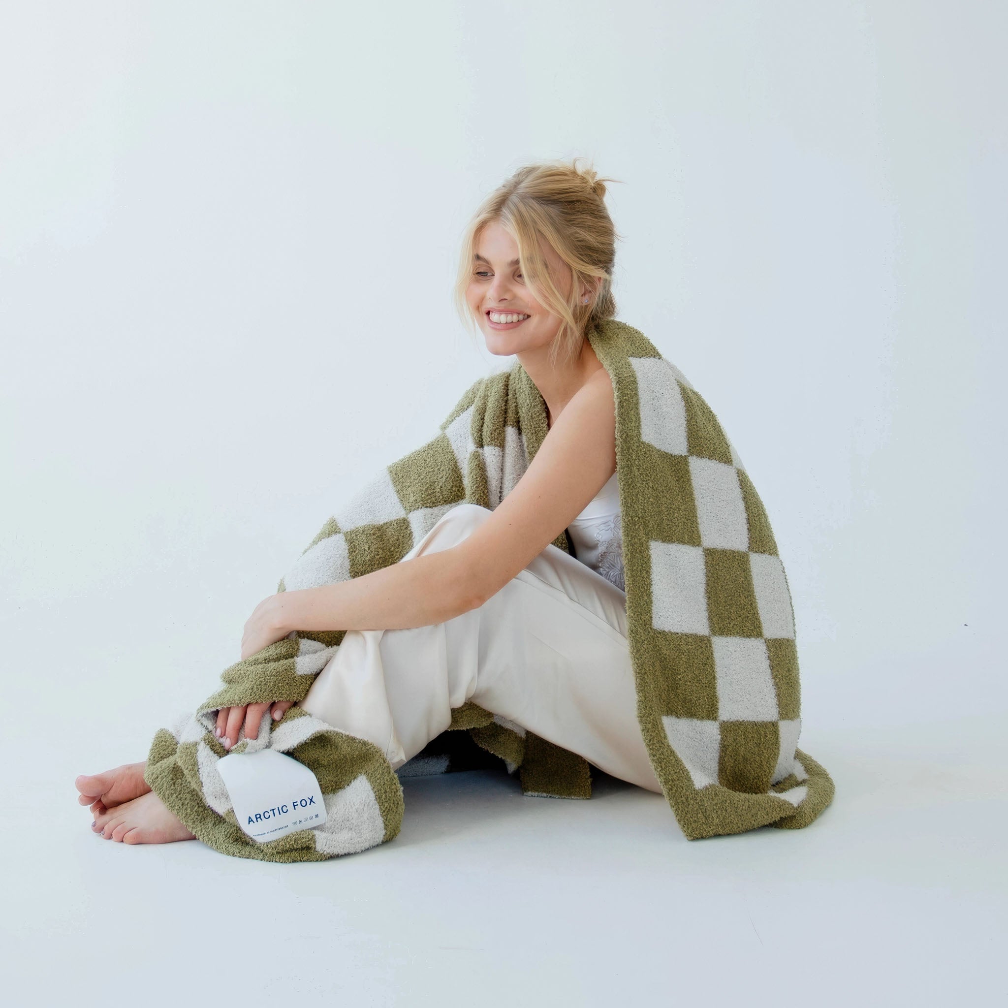 Model wrapped in a moss green and white checkered blanket on a light background