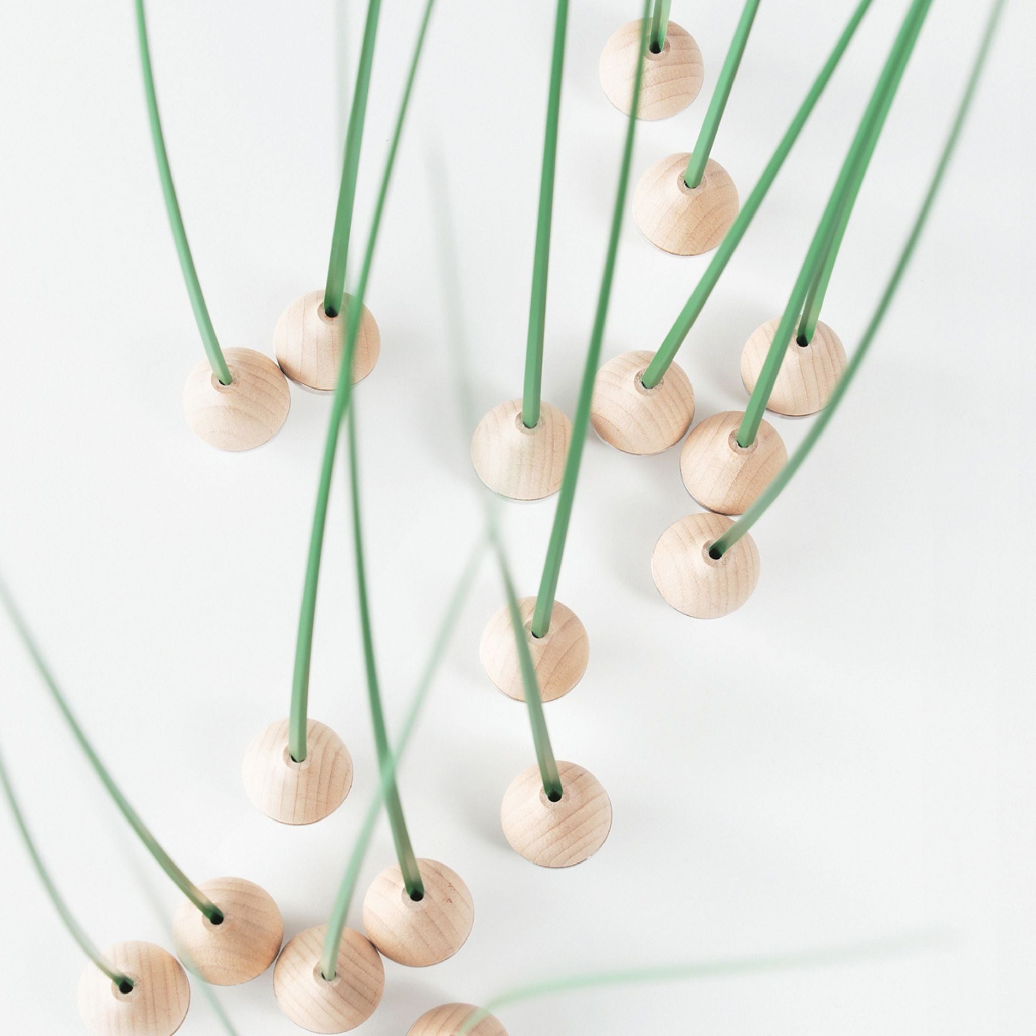 Multiple KUSA objects by switch shown in motion, with green flexible stems and light wooden bases creating a sculptural field effect