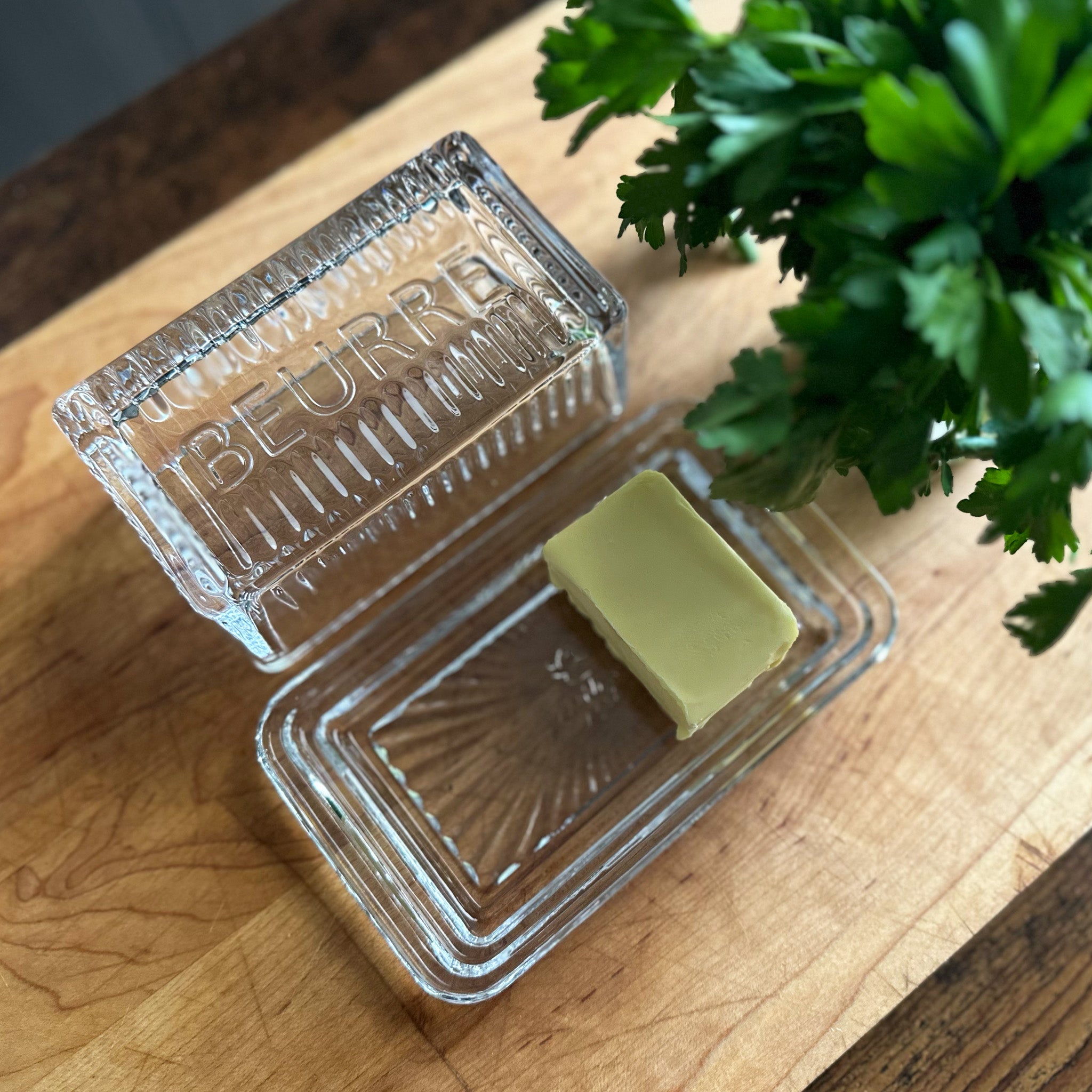 Block of butter in a glass container on a wooden surface with a plant in the background