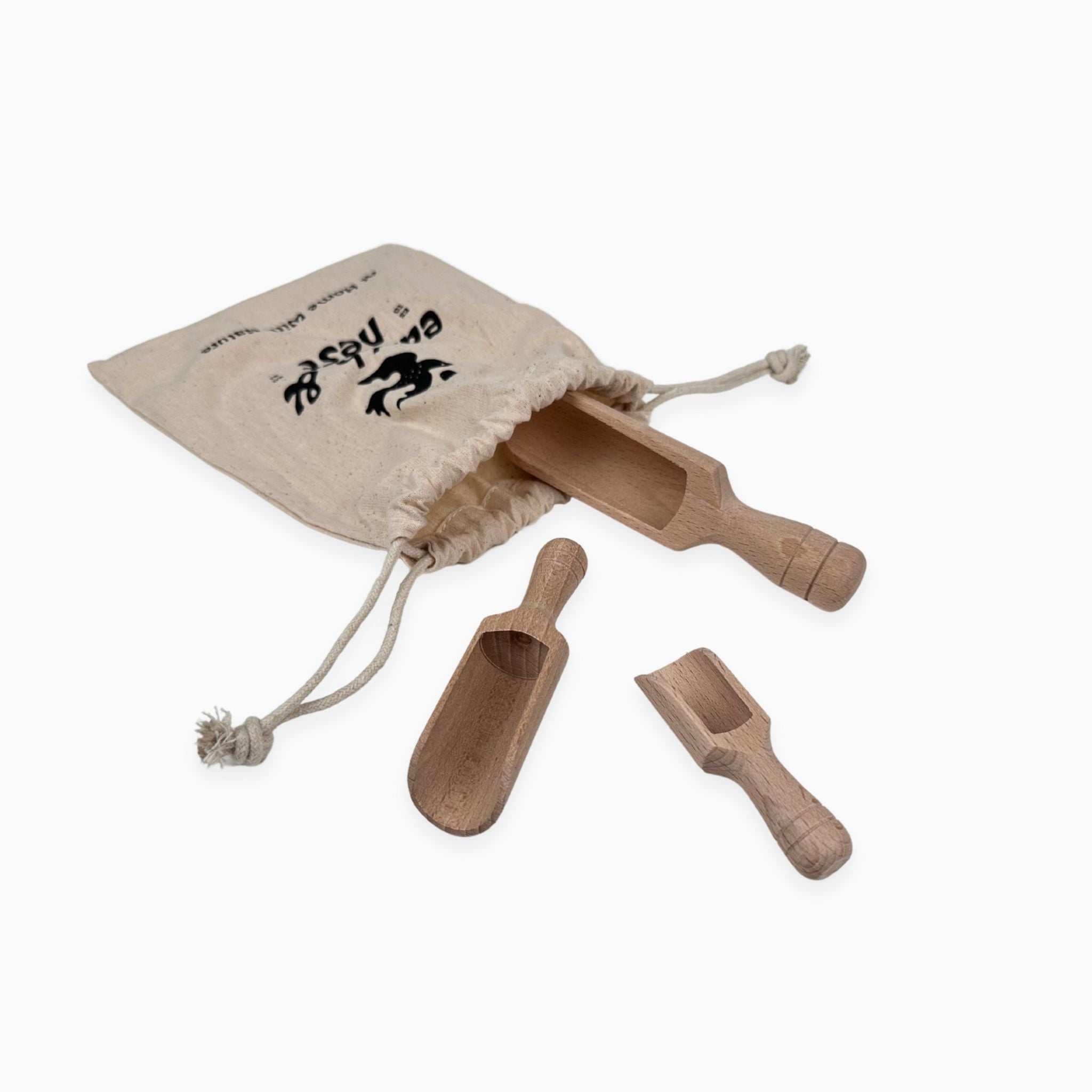 Set of three wooden scoops in varying sizes partially tucked into a cotton drawstring bag with printed Earth + Nest branding, displayed on a white background.