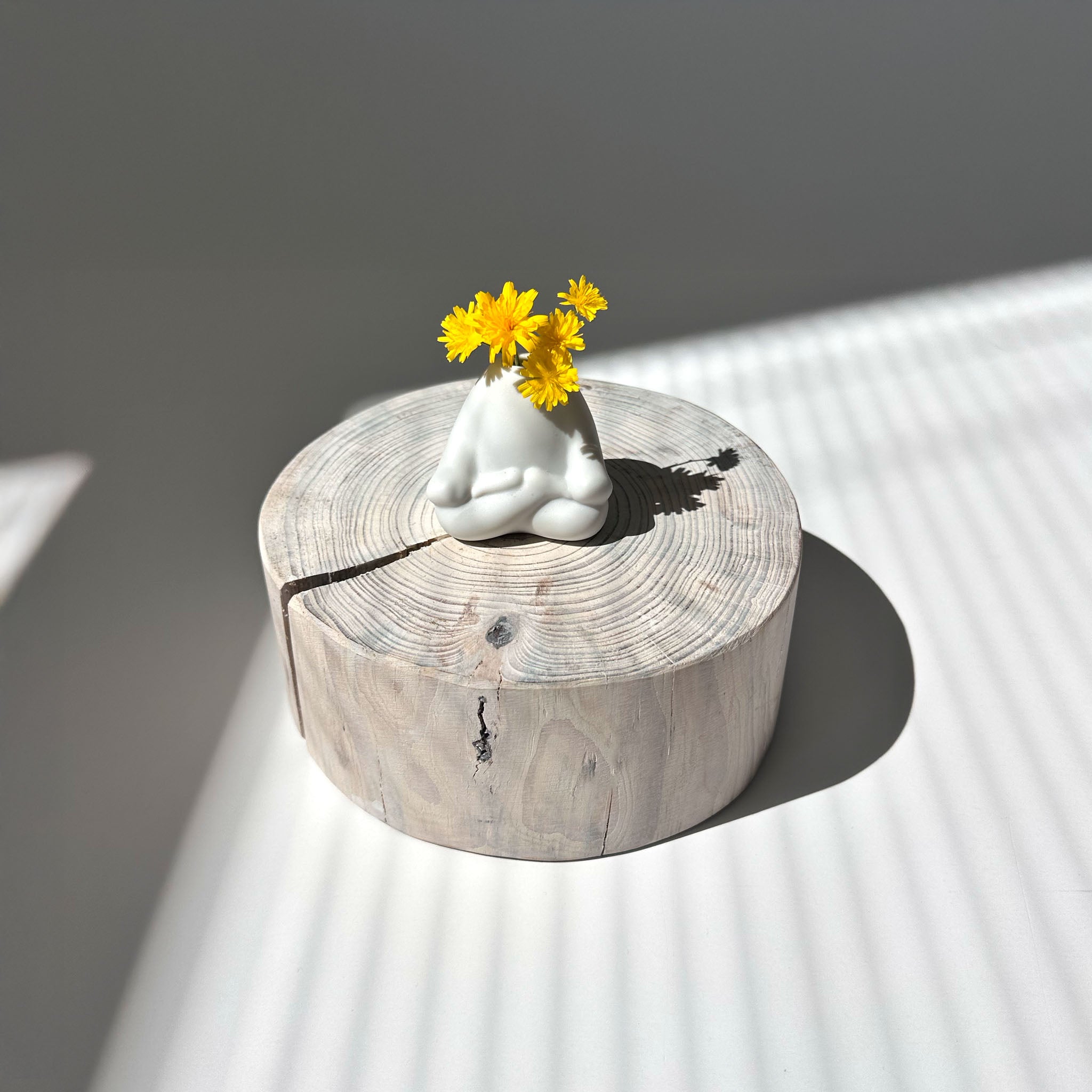 White ceramic mini vase of a person in a meditative pose with yellow flowers on a wooden pedestal against a neutral background.