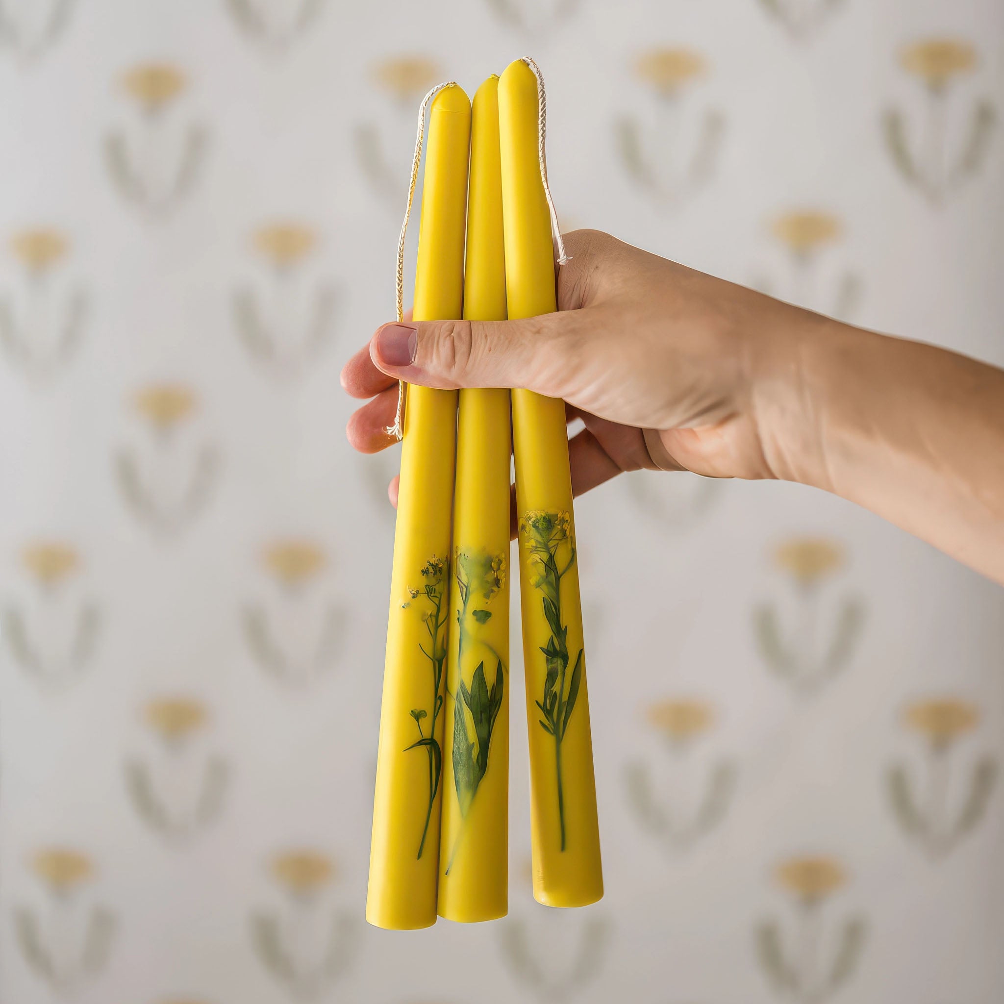 Image of someone holding three yellow floral inlaid tapered candles