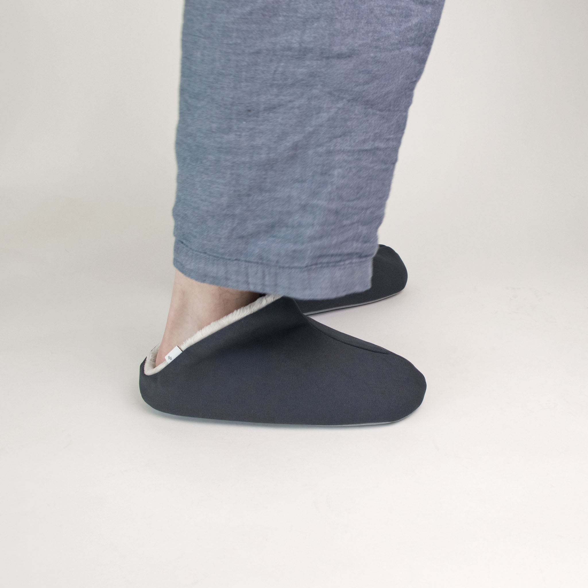 Person wearing a dark grey slipper on a light gray background
