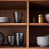 Wooden shelves with various ceramic and glass items including black glasses and white bowls.