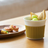Green and white ceramic cup with snacks on a wooden table