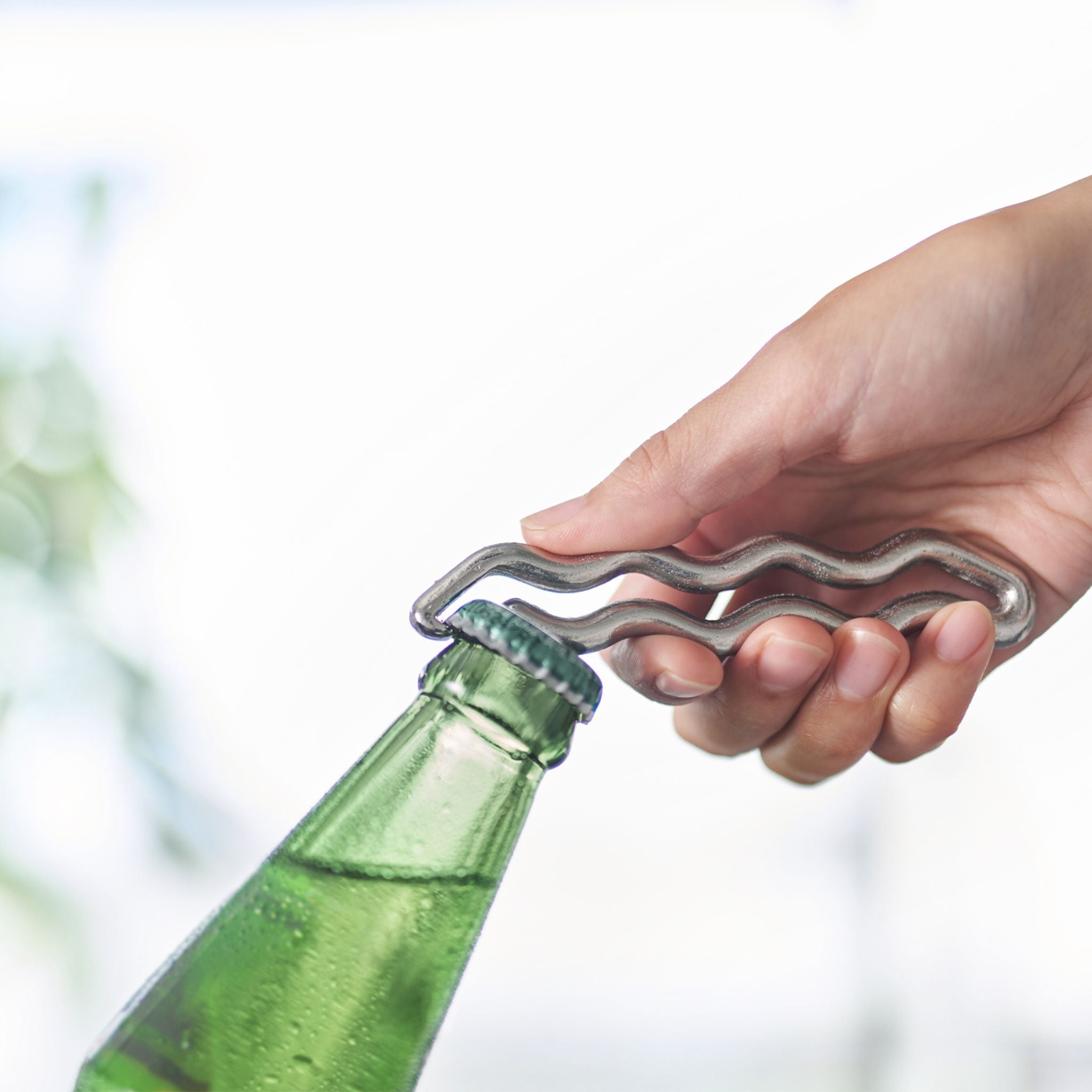Hand using the silver WARP opener on a green bottle with a blurred background