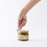 Hand using the silver WARP opener to open a jar of smoked sardines on a white background