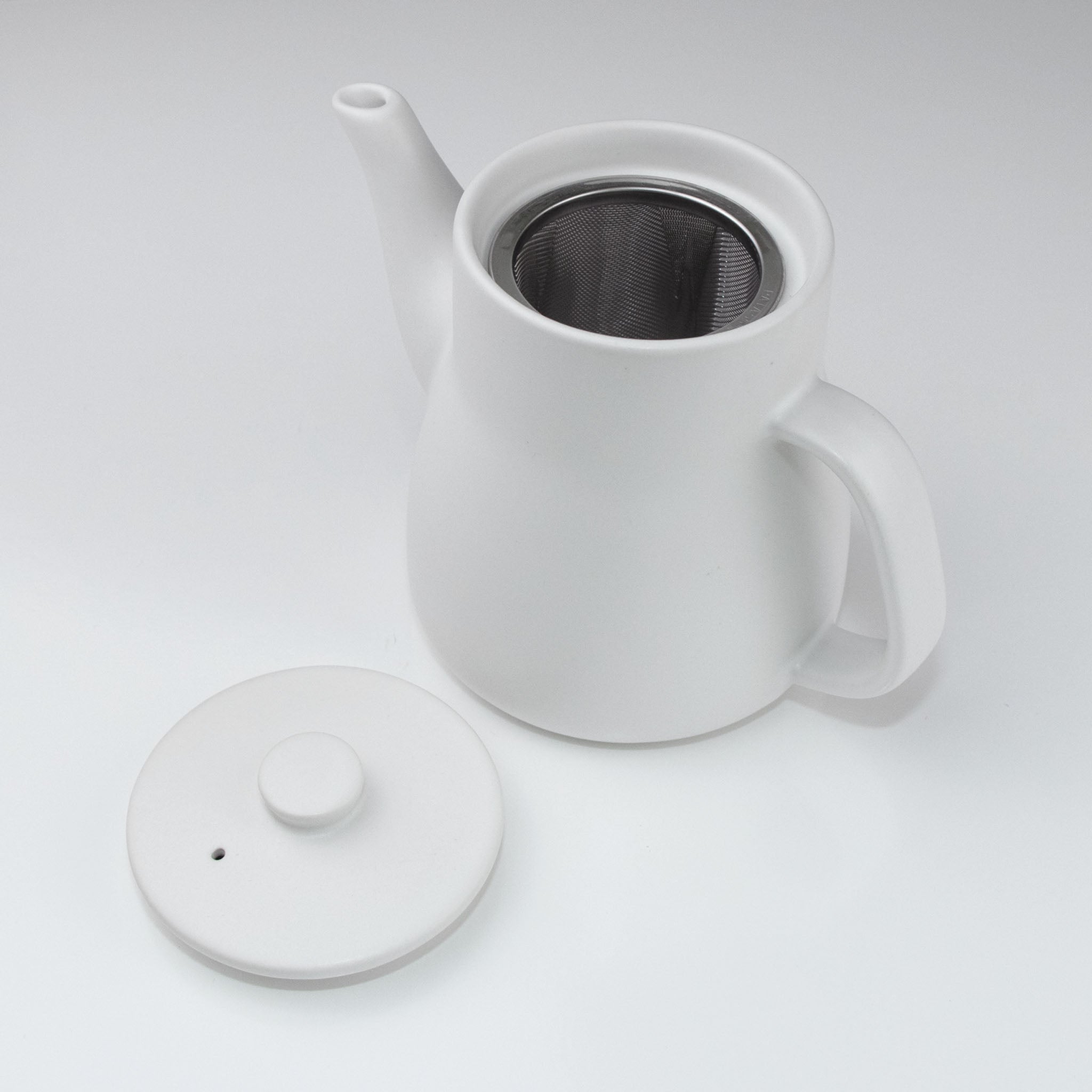 White ceramic teapot with a lid on a light gray background