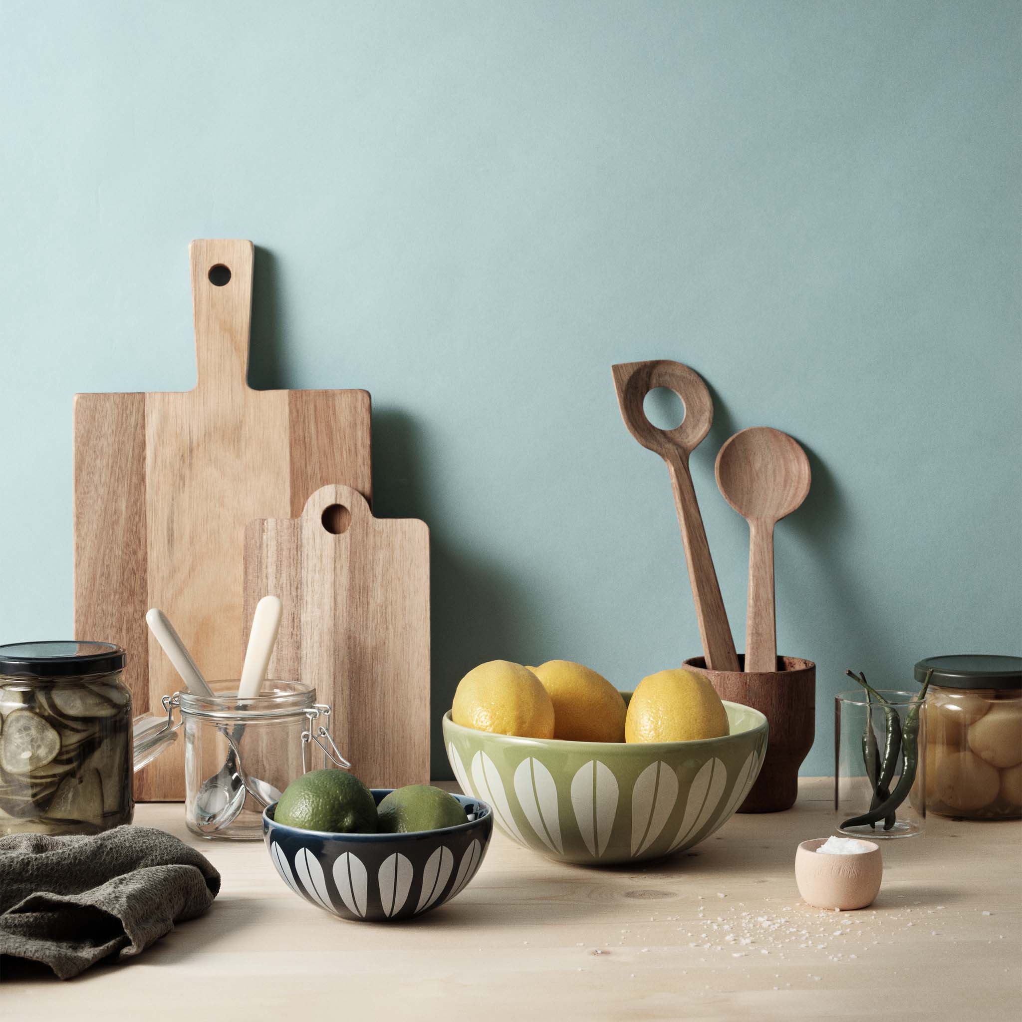 Green and blue Lucie Kaas Lotus Bowls styled in a kitchen scene with lemons, limes, cutting boards, and wooden utensils, highlighting the iconic white lotus pattern.