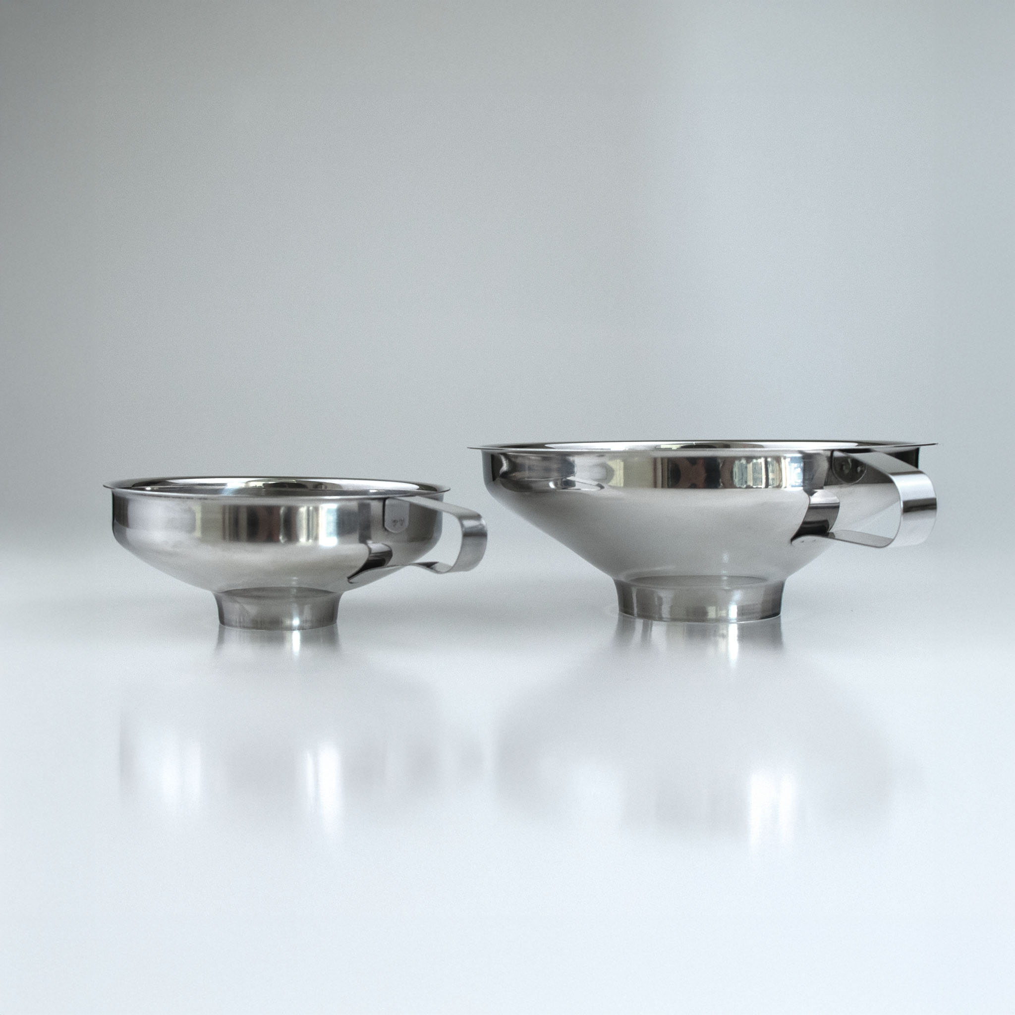 Two metal funnels on a reflective surface with a light gray background
