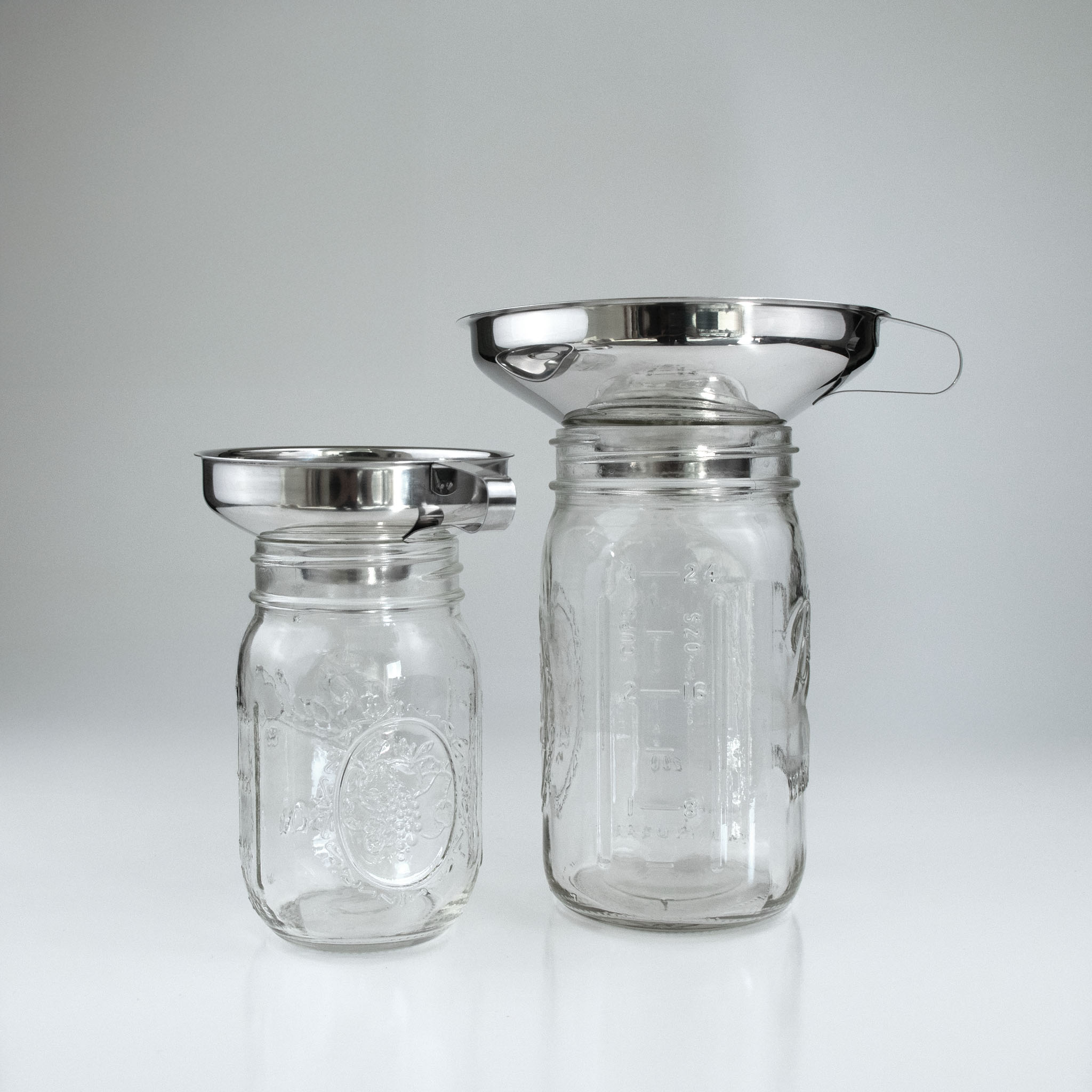 Two glass jars with stainless steel funnels on a white background