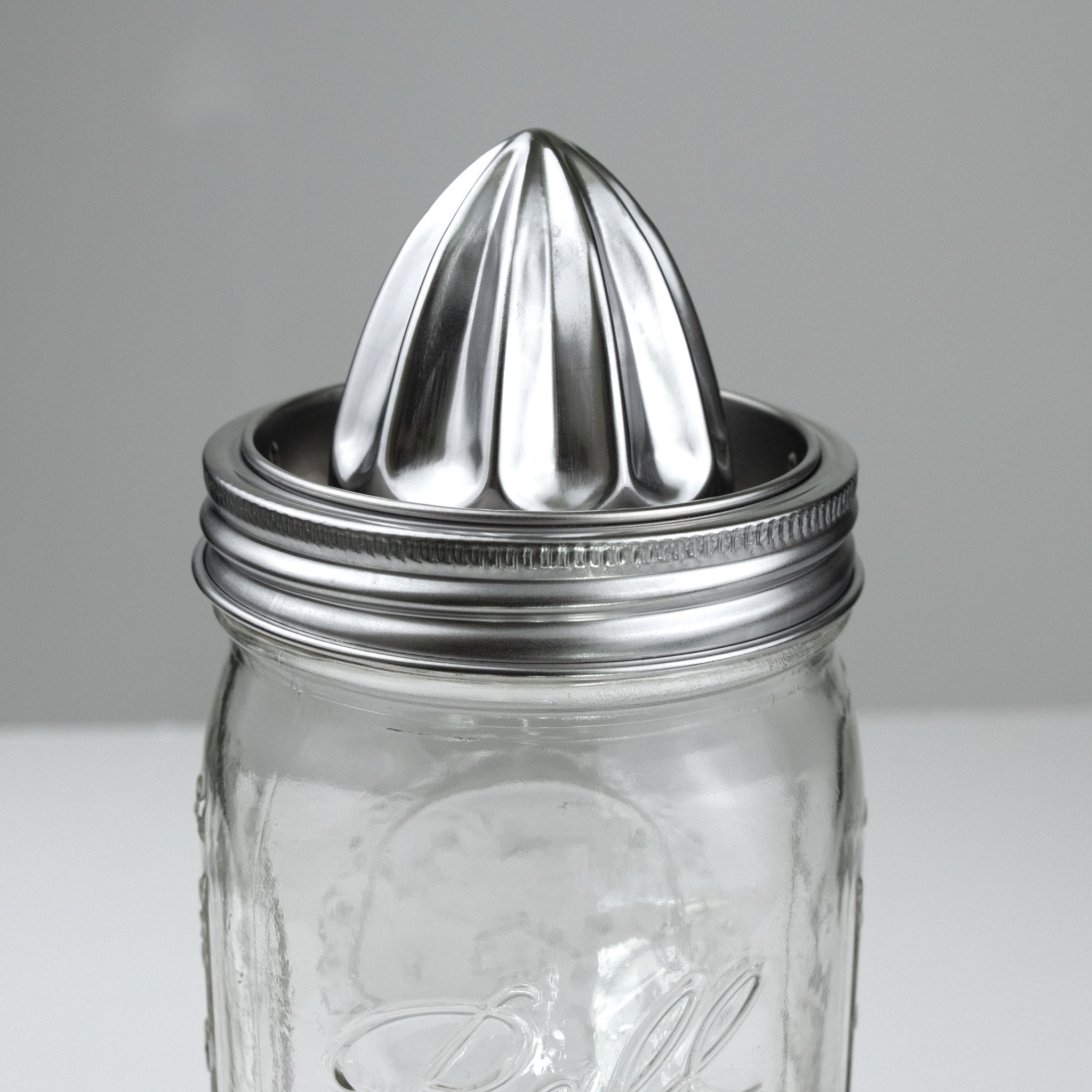 Clear mason jar with a stainless steel citrus juicer on a gray background