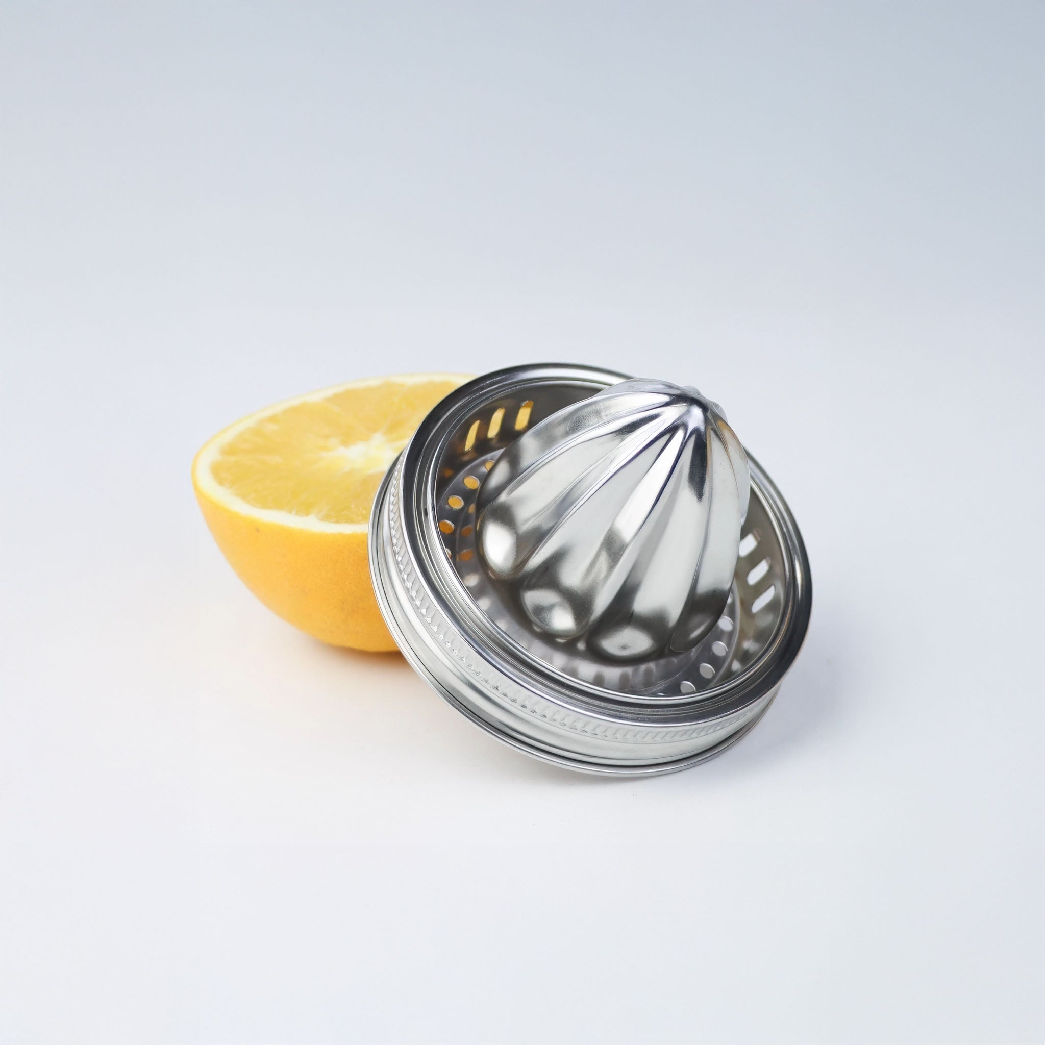 Stainless steel citrus juicer next to a halved lemon on a light gray background