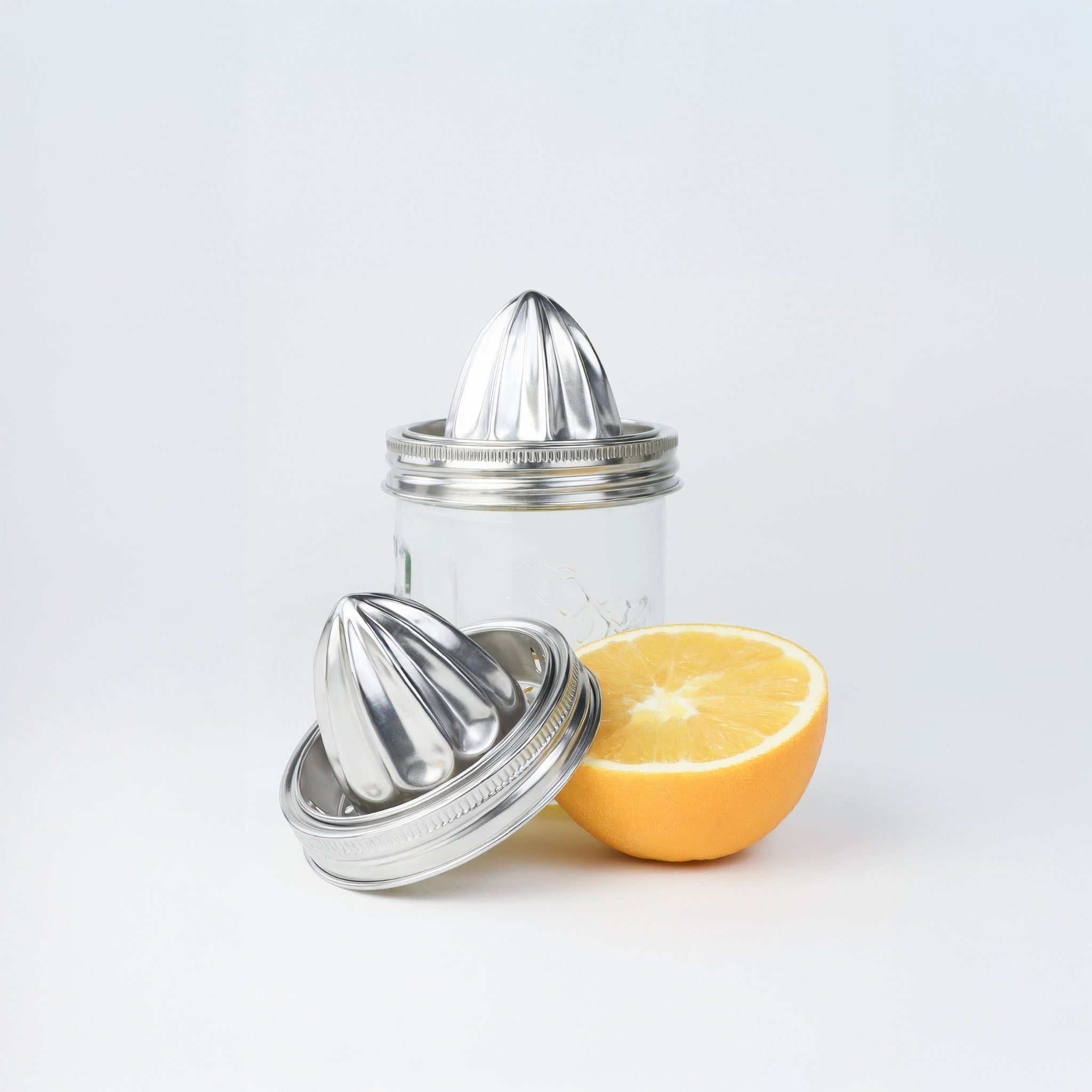 Clear glass citrus juicer with stainless steel juicer and half a lemon on a light gray background